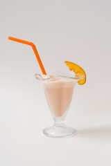 Milkshake with nectarines in a glass with a plastic orange tube in it on a white background. The concept of healthy and delicious food