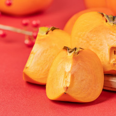 Fresh beautiful sliced sweet persimmon kaki isolated on red table background and bamboo sieve, Chinese lunar new year design concept, close up.