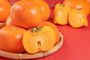 Fresh beautiful sliced sweet persimmon kaki isolated on red table background and bamboo sieve, Chinese lunar new year design concept, close up.