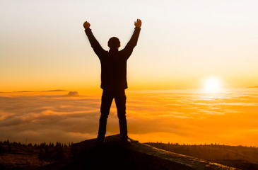 Fototapeta premium Silhouette of success and serenity young man standing on a rock in the mountains at sunset. 