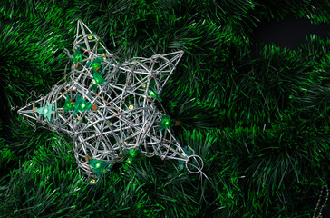 Silver vine star decorated with a Christmas tree garland on a green tinsel background
