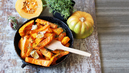 Baked pumpkin slices in a pan with herbs and garlic. Autumn lunch. Vegan food. Healthy snack.