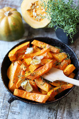 Baked pumpkin slices in a pan with herbs and garlic. Autumn lunch. Vegan food. Healthy snack.