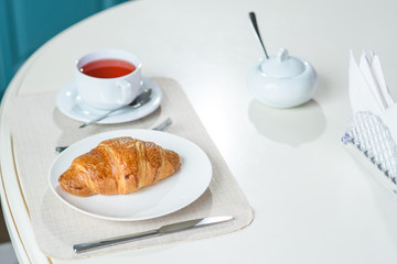 Fruit tea and delicious fresh croissant on the table in a cozy coffee shop