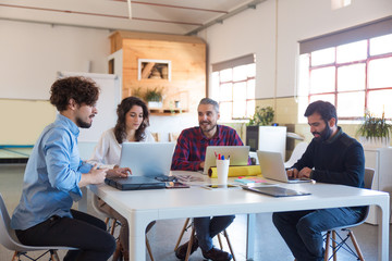 Creative group working on startup, using laptops in modern co-working with potted plant. Business...