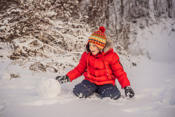Fototapeta na wymiar Cute boy in red winter clothes builds a snowman. Winter Fun Outdoor Concept