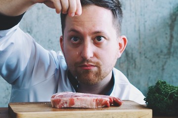 man putting salt on meat slice in kitchen