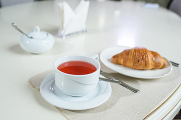 Fruit tea and delicious fresh croissant on the table in a cozy coffee shop