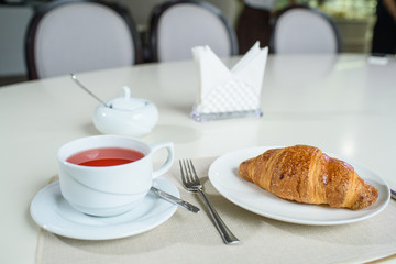 Fruit tea and delicious fresh croissant on the table in a cozy coffee shop