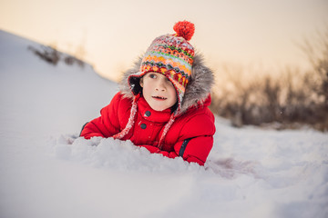 Fototapeta na wymiar Boy in red fashion clothes playing outdoors. Active leisure with children in winter on cold days. Boy having fun with first snow. Happy little kid is playing in snow, good winter weather