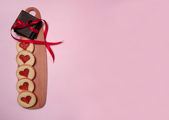 The Concept Of Valentine's Day. Homemade cakes for the holiday.  Cookies in the shape of hearts, chocolate tied with a red ribbon on a wooden Board on a pink background. Free space for your text.