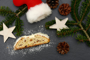 christmas stollen with fir branch, santa claus shoe and stars lying on black shale at christmas time