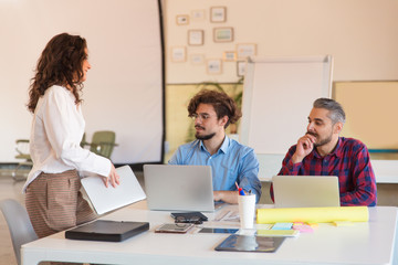 Creative group with laptops gathering in meeting room. Business colleagues in casual sitting together in contemporary office space. Brainstorming or teamwork concept