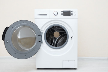 modern unloaded washing machine with open door and screen on control panel on wooden floor against beige wall