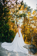 The bride in a white dress stands in the autumn park