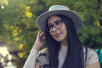 Close up of happy emotionally brunette woman with long hair and hat, smiling at camera. Beautiful model with perfect makeup after salon, posing in park. Concept of fashion and beauty.