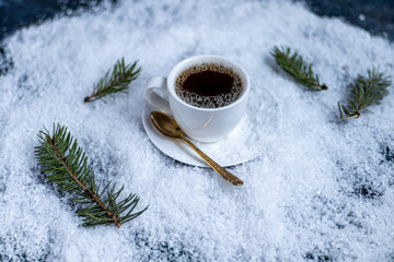 White cup with hot coffee. Stands in artificial snow. Near a branch of spruce. New Year's and Christmas.