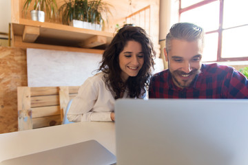 Two friendly coworkers using laptop, watching content together. Business colleagues in casual working together in contemporary office space. Working together concept