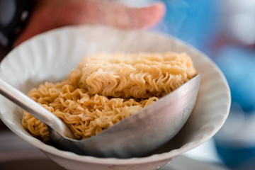 Instant noodles were blanched in a boiling hot water pot and being scooped up using a dipper to a bowl.morning light.