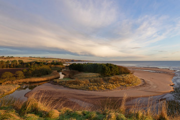 Obraz premium The mouth of the Lunan Water, with the winding river gently running into the North Sea on the East Coast of Scotland on a December morning.