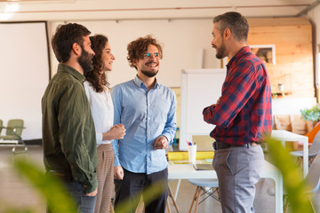 Fototapeta premium Startup team reporting to leader, smiling, laughing. Business colleagues in casual working together in contemporary office space. Team meeting concept
