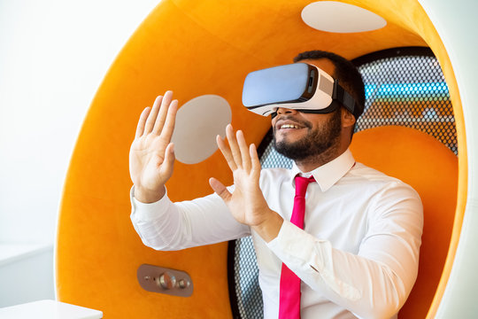Happy businessman using VR headset. Young African American businessman sitting in spherical chair and using VR headset. Technology concept