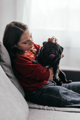Side view of young woman stroking pug dog on sofa