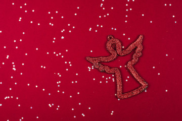 Obraz na płótnie Canvas Red shiny symbol of angel and Christianity on a red background with silver stars of confetti. Symbol of the Catholic Christmas and New Year. Flat lay, copyspace