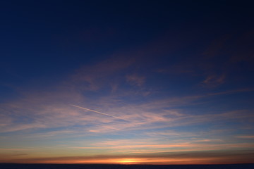 Airplane trail in the blue sky in white cirrus clouds in winter at sunset