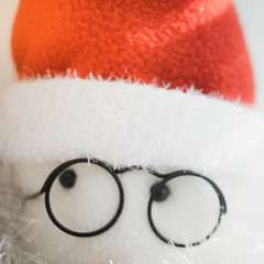 Soft toy abstract Santa Claus face in black round glasses and red hat, closeup eyes.