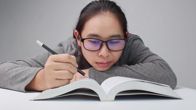Young woman with glasses drawing a line and writing short summary while reading a book at library.