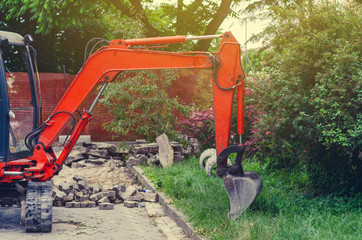 Small excavator on sidewalk near lawn. Repair in city, urban