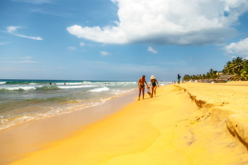 young tanned family walk hand in hand with little daughter on sandy shore of tropical ocean beach, Sri Lanka.