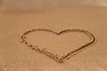 Hand-drawn heart shape symbol of love on wet yellow sand on beach, copy space