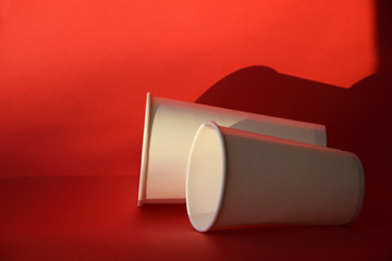 Two empty paper glasses lie on a red background, mock up. Eco paper glass containers for drink and beverage on table. Eco-Friendly disposable tableware concept.