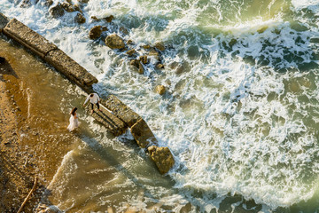 Sea view from above - happy wedding couple by the foamy sea waves. Romantic wedding ideas by the sea. Never-ending beauty of nature.