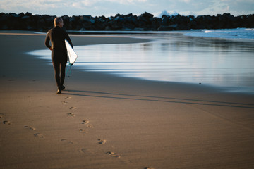 Adult surfer walking on Zurriola Beach seashore
