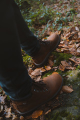 Feet wearing black jeans and classic brown boots walking on top of fallen leaves