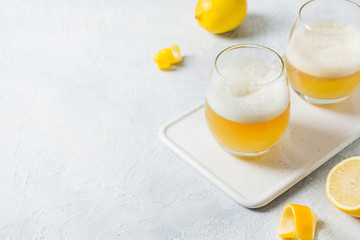 Two whiskey sour cocktails with ingredients, lemon juice, sugar syrup and egg white in glass on white. Horizontal orientation.