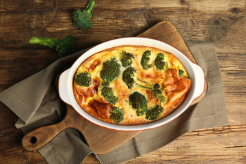 Tasty broccoli casserole in baking dish on wooden table, flat lay