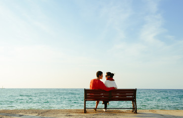young couple looking at each other on bench by the Aegean sea