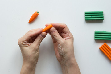 Woman hands making small carrot polymer clay on white background