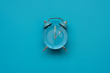 Time to eat. Plate with cutlery as clock on blue background. Top view. Flat lay. Weight loss and...