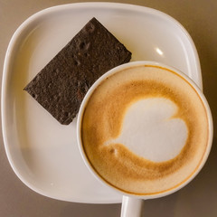 A Cup of hot latte art coffee with a bar of brownie