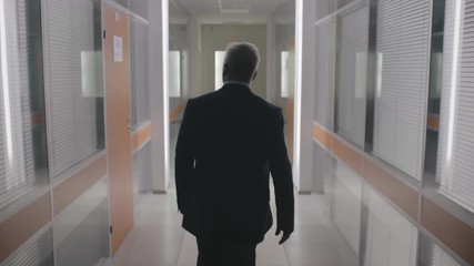 Silhouette of confident senior businessman wearing formal suit walk through office hall corridor of business center at evening time after work. Boss CEO entrepreneur employer finishes work day