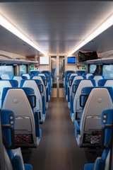 Inside cabin of modern express train.  Empty class two car with comfortable blue chairs, glass doors, monitor and safety equipment. Carriage interior.