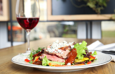 Delicious salad with roasted meat and vegetables served on wooden table indoors. Space for text