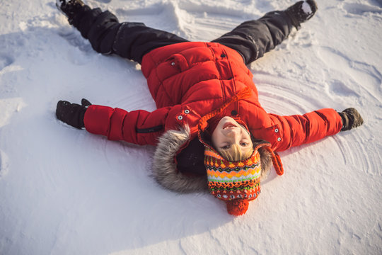 A child, a boy, lies on the snow, makes a snow angel with his arms and legs, emotions, laughs