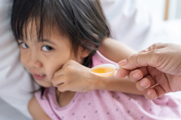 Unhappy ill Asian girl when taking medicine syrup from her mother