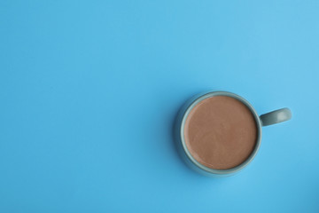 Delicious cocoa drink in cup on light blue background, top view. Space for text